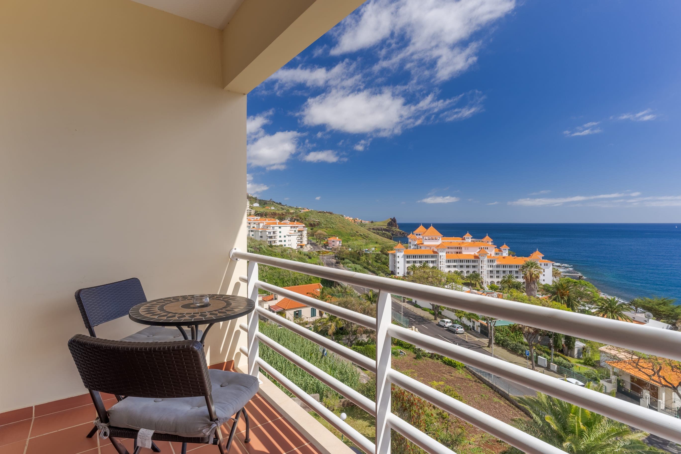 Balcony with bistro table and chairs overlooking coastline and blue sky