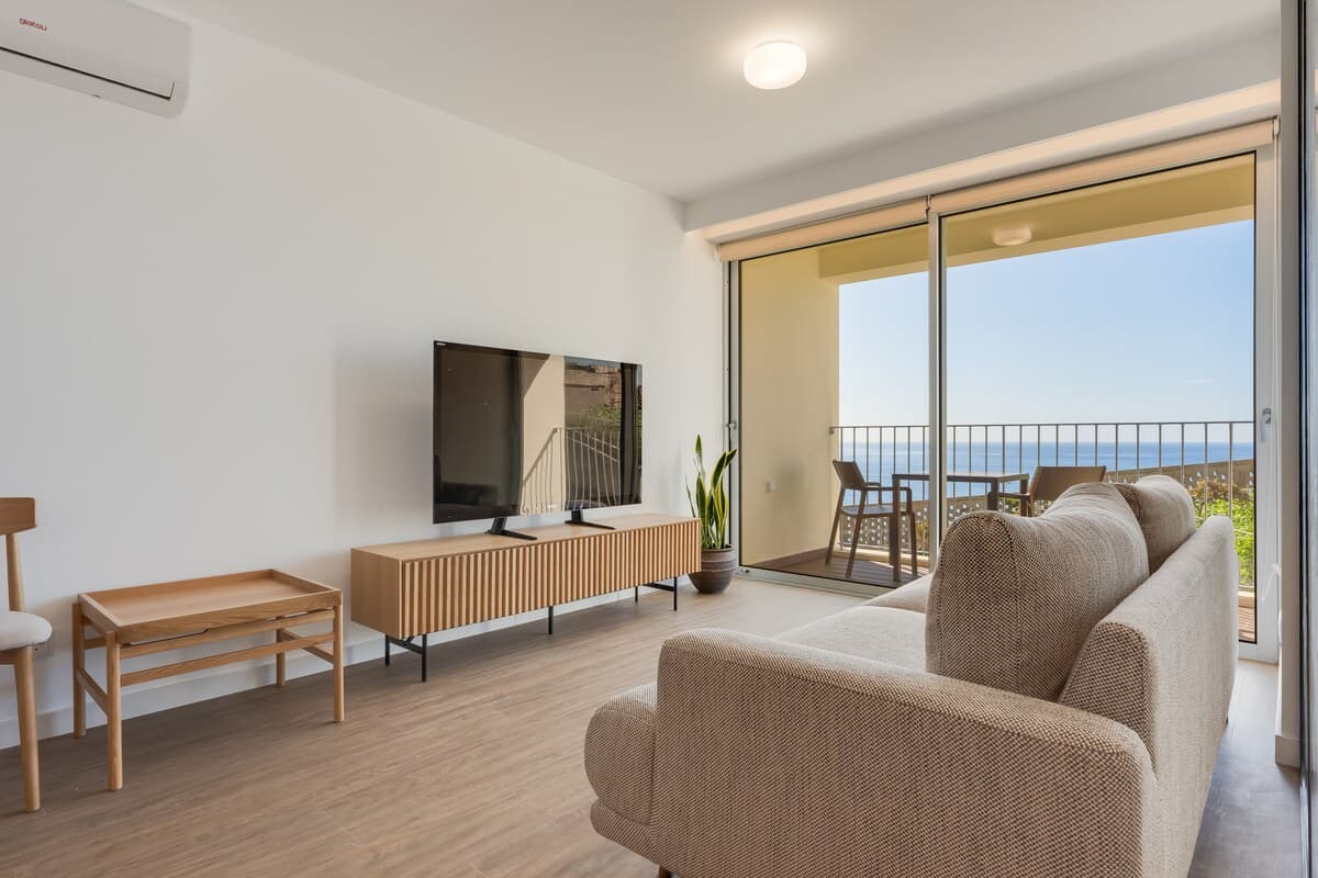 Sala confortável com TV e ar condicionado, aberta para uma varanda com espaço para relaxar.